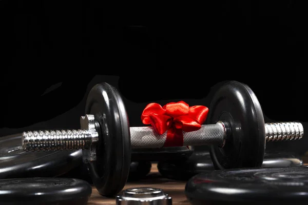 Hediye: Koyu ahşap bir masada kırmızı kurdeleyle bağlanmış halterler ve spor malzemeleri.