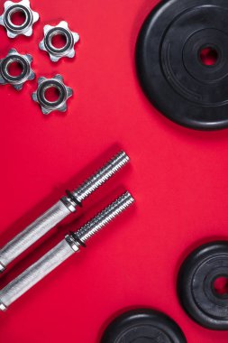 Fitness ya da vücut geliştirme. Kırmızı arka planda spor malzemeleri, halter, dambıl, üst manzara.