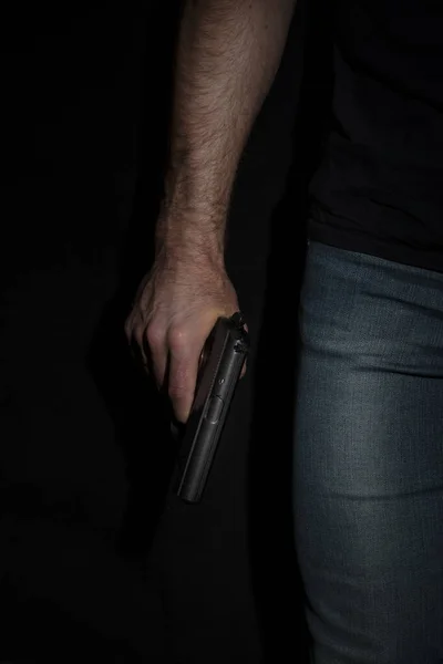 Ein Mann mit einer Waffe in der Hand auf schwarzem Hintergrund. Killer mit Waffe — Stockfoto