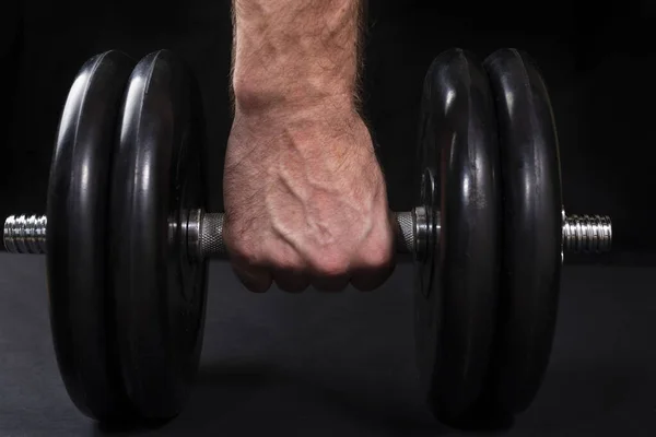 Male hand holds steel type-setting dumbbell, sports training with weight on a black background