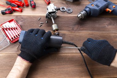 Usta bozuk bir elektrikli aleti tamir eder: matkap, tahta bir masa üzerinde kesici. Elektrikli Araç Tamir Dükkanı