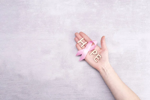 医疗保健和医学概念- -女性手握粉色乳腺癌意识带和灰色背景下的希望字样 — 图库照片