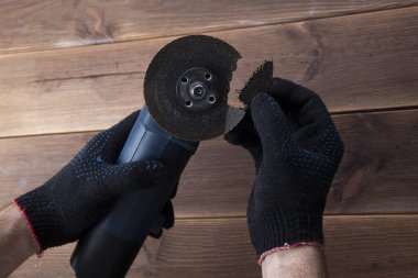 Ahşap bir masada çalışan eldivenlerin elinde kırık bir bıçakla öğütücü. Elektrikli alet kullanmanın tehlikesi