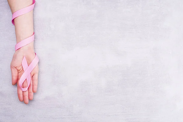 Concepto de salud y medicina: la mano femenina sostiene la cinta rosa de conciencia sobre el cáncer de mama en un fondo gris con lugar para el texto — Foto de Stock