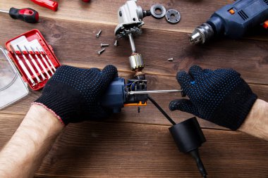 Usta bozuk bir elektrikli aleti tamir eder: matkap, tahta bir masa üzerinde kesici. Elektrikli Araç Tamir Dükkanı