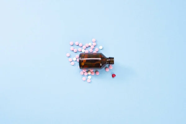 Una foto de tabletas vertidas de un frasco de vidrio ámbar. Pastillas para medicamentos farmacéuticos, pastillas del corazón sobre un fondo azul — Foto de Stock