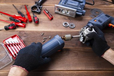 Usta bozuk bir elektrikli aleti tamir eder: matkap, tahta bir masa üzerinde kesici. Elektrikli Araç Tamir Dükkanı