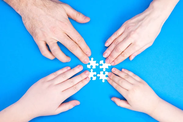 Las manos del hombre, la mujer y los niños recogen rompecabezas sobre un fondo azul. Imagen conceptual de la cooperación conjunta en la familia. Vista desde arriba — Foto de Stock