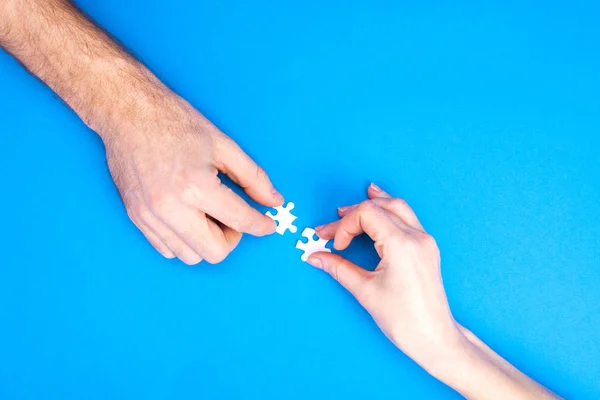 Las manos del hombre y la mujer recogen rompecabezas sobre un fondo azul. Imagen conceptual de la cooperación conjunta en la familia. Vista desde arriba — Foto de Stock