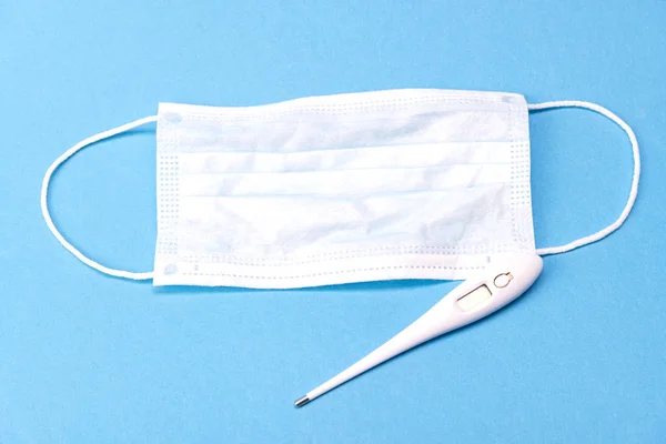 Mavi arka planda tıbbi dijital termometre ve tıbbi maske. Tıbbi konsept