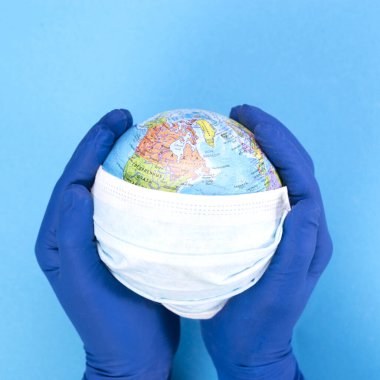 Küredeki tek kullanımlık tıbbi maske mavi arka plandaki bir doktorun elinde, Dünya 'nın modeli. Salgın konsepti. KOVID-19, koronavirüs. Hastalığın küresel salgını..