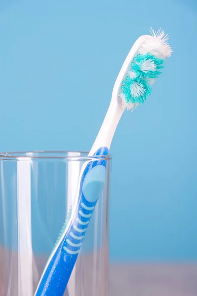 Ancienne brosse à dents usagée dans une tasse en verre sur fond bleu gros plan — Photo