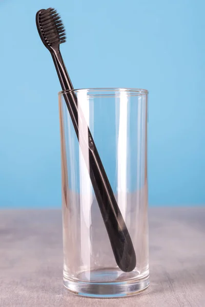 Brosse à dents noire dans une tasse en verre se tient sur une table sur un fond bleu — Photo
