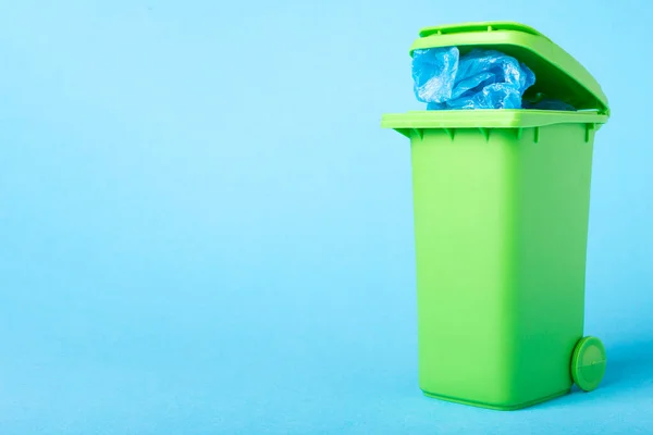 Grüner Mülleimer mit Polyethylenabfällen auf blauem Hintergrund mit Platz für Text — Stockfoto