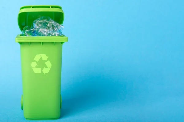 Bote de basura verde con residuos de plástico y el icono de reciclaje en un fondo azul con lugar para texto — Foto de Stock