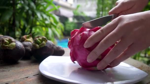 Menina corta fruta de dragão no quadro de uma grande mão na piscina de fundo — Vídeo de Stock