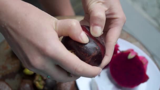 Das Mädchen enthüllt eine Mangostane im Rahmen große Hände im Hintergrund liegen — Stockvideo