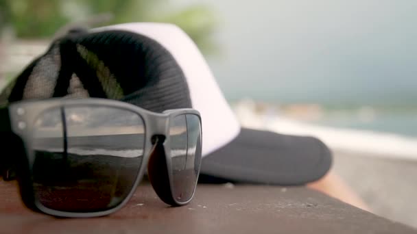 Auf dem Tisch liegen eine Mütze und Gläser, in denen die Wellen des Ozeans — Stockvideo