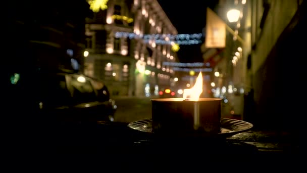 Uma vela queima à noite na rua, as luzes estão para trás, e os carros estão dirigindo — Vídeo de Stock