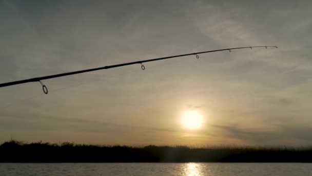 Pescador captura peixe em um lago ao pôr do sol, close-up haste de pesca girando — Vídeo de Stock
