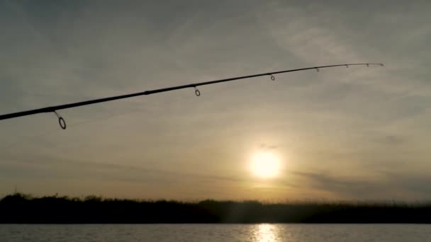 Visser vangt vis op een meer bij zonsondergang, close-up vishengel draaiend — Stockvideo