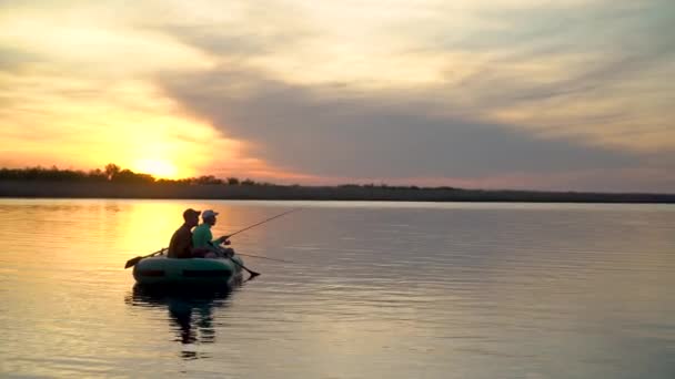 Två fiskare i solnedgångens strålar fångar fisk från en uppblåsbar båt — Stockvideo