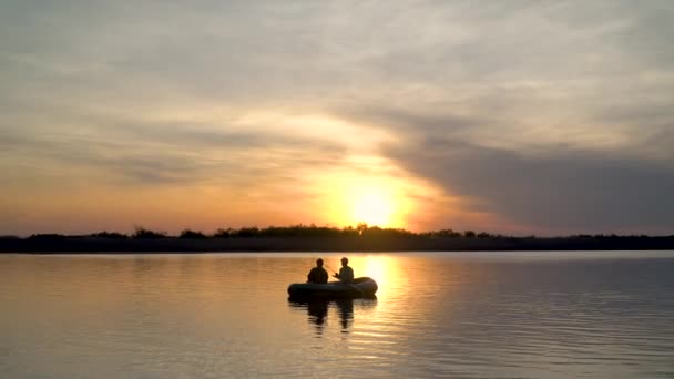 Dois pescadores nos raios do pôr-do-sol capturam peixes de um barco inflável — Vídeo de Stock