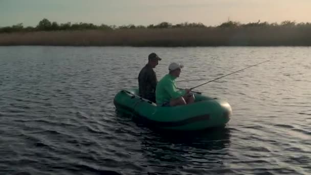 Två fiskare i solnedgångens strålar fångar fisk från en uppblåsbar båt — Stockvideo