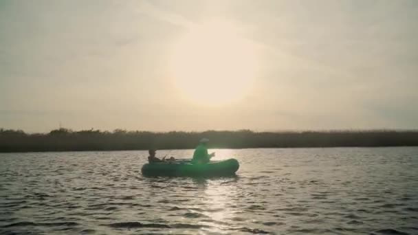 Dois pescadores nos raios do pôr-do-sol capturam peixes de um barco inflável — Vídeo de Stock