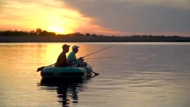 Dois pescadores nos raios do pôr-do-sol capturam peixes de um barco inflável — Vídeo de Stock