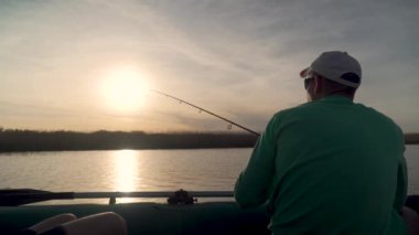 Gün batımında gölde balık tutan balıkçı, arkadan gören.