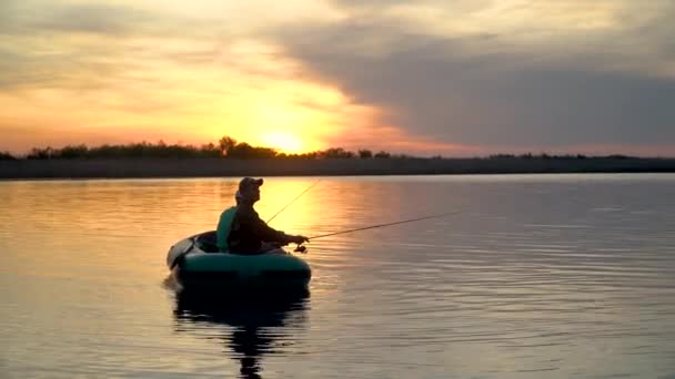 Δύο ψαράδες στις ακτίνες του ηλιοβασιλέματος πιάνουν ψάρια από ένα φουσκωτό σκάφος. — Αρχείο Βίντεο