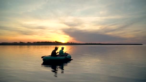 Два рыбака в лучах заката ловят рыбу с надувной лодки — стоковое видео