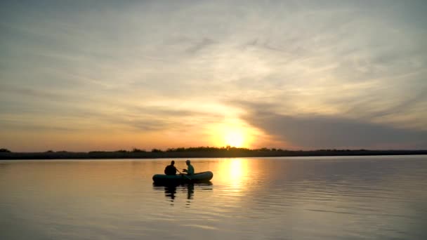 Δύο ψαράδες στις ακτίνες του ηλιοβασιλέματος πιάνουν ψάρια από ένα φουσκωτό σκάφος. — Αρχείο Βίντεο