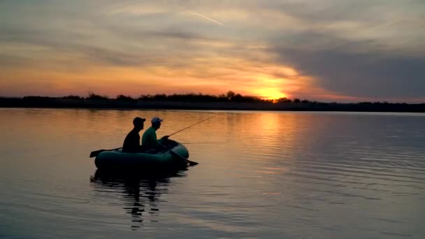 Dois pescadores nos raios do pôr-do-sol capturam peixes de um barco inflável — Vídeo de Stock