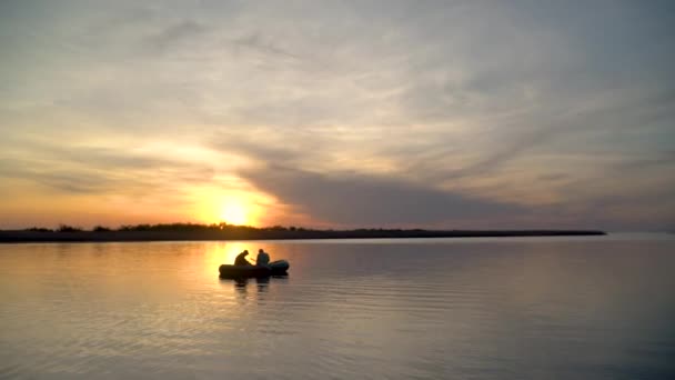 Dois pescadores nos raios do pôr-do-sol capturam peixes de um barco inflável — Vídeo de Stock