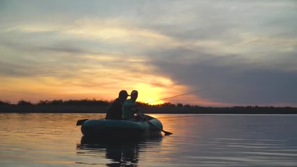 Dois pescadores nos raios do pôr-do-sol capturam peixes de um barco inflável — Vídeo de Stock