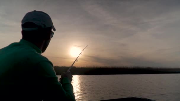 Rybář při západu slunce rybaří na jezeře, pohled zezadu — Stock video