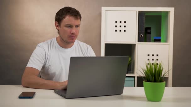 Чоловік сидить за столом, працюючи на ноутбуці — стокове відео