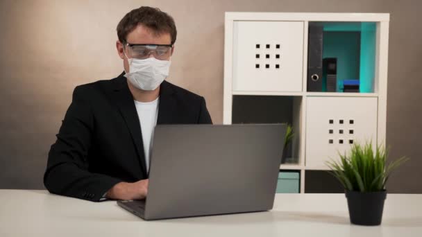 Man werkend op laptop in beschermende bril en masker — Stockvideo