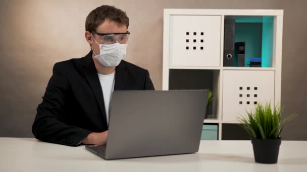 Muž pracující na notebooku v ochranných brýlích a masce — Stock video