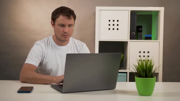 Мужчина сидит за столом с ноутбуком и разговаривает по телефону — стоковое видео
