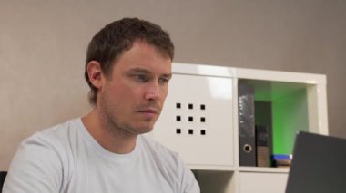 Bir adam dizüstü bilgisayarla masada oturuyor ve telefonla konuşuyor.