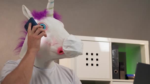 Un hombre con una máscara de unicornio y una máscara protectora para una computadora portátil — Vídeo de stock