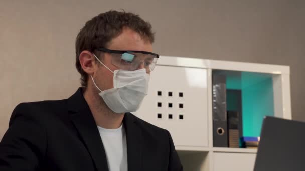 Man werkend op laptop in beschermende bril en masker — Stockvideo