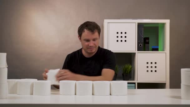 Egy férfi épít az asztalra egy piramist WC papírból. — Stock videók