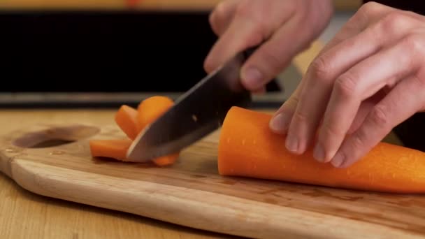 Een man snijdt een wortel op een snijplank — Stockvideo