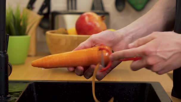 Un hombre limpia una zanahoria en la cocina — Vídeo de stock