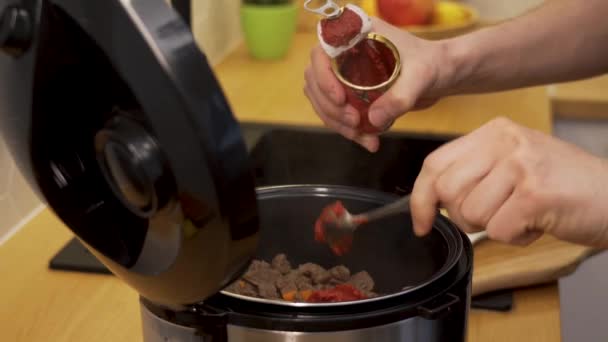 Mannen sätter tomatpuré i den långsamma spisen — Stockvideo