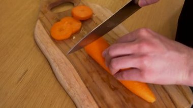 Bir adam kesim tahtasıyla havuç kesiyor.